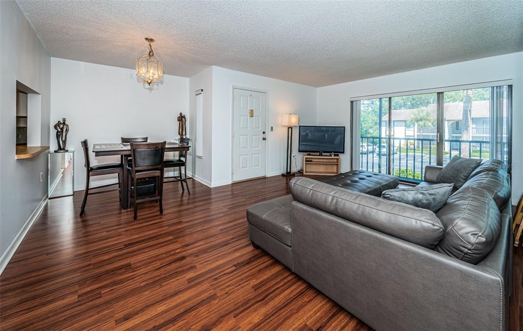 A living and dining area with wood-look flooring, a gray sectional, and a sliding glass door — 2522 PINE RIDGE WAY S UNIT A2, PALM HARBOR, FL