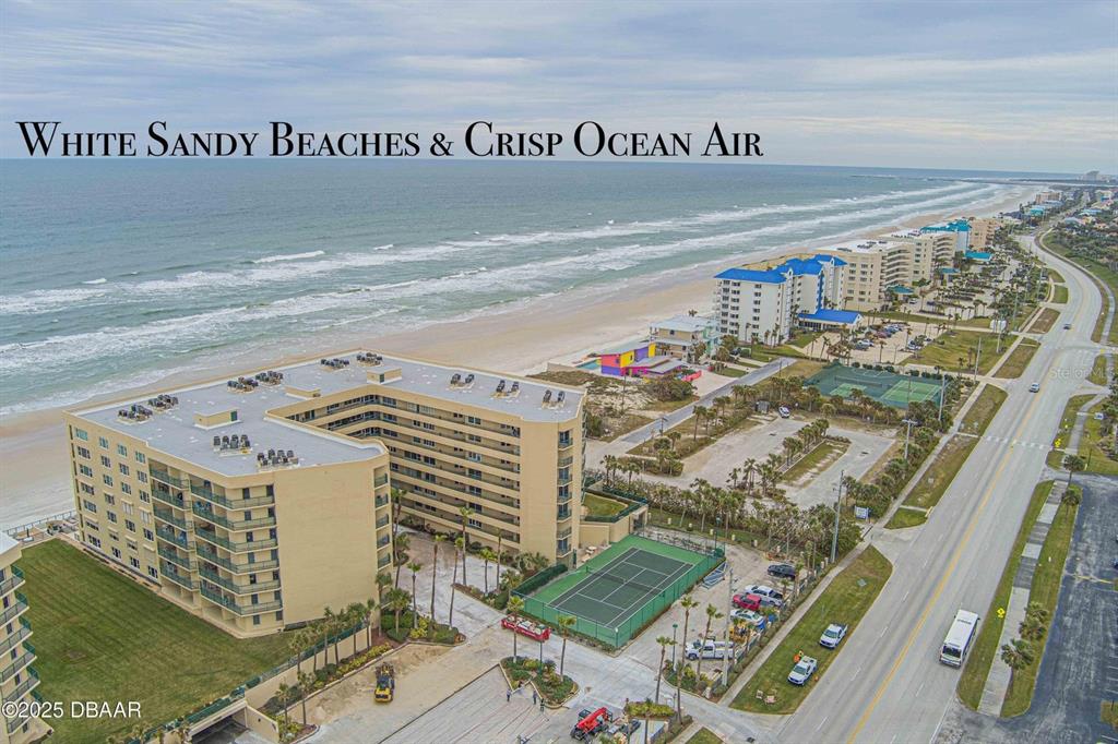An aerial view shows a multi-story tan apartment building next to a beach and tennis court — 4575 S ATLANTIC AVENUE UNIT 6607, PONCE INLET, FL
