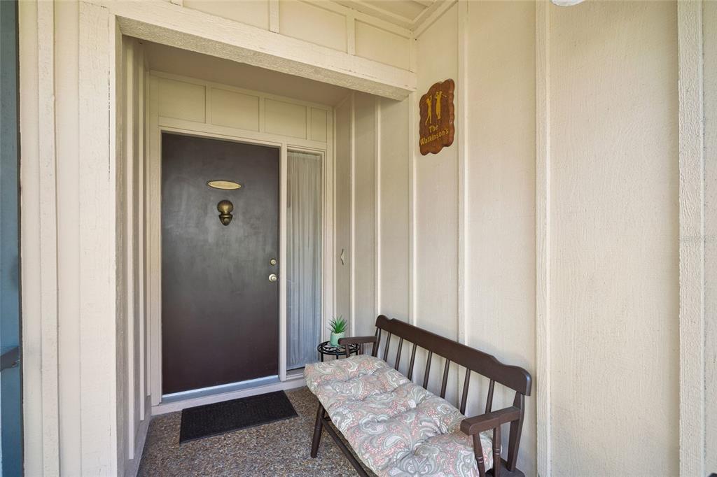 A covered entryway features a dark brown front door, a wooden bench, and a wall sign — 4688 OAK HOLLOW DRIVE UNIT 25, SARASOTA, FL