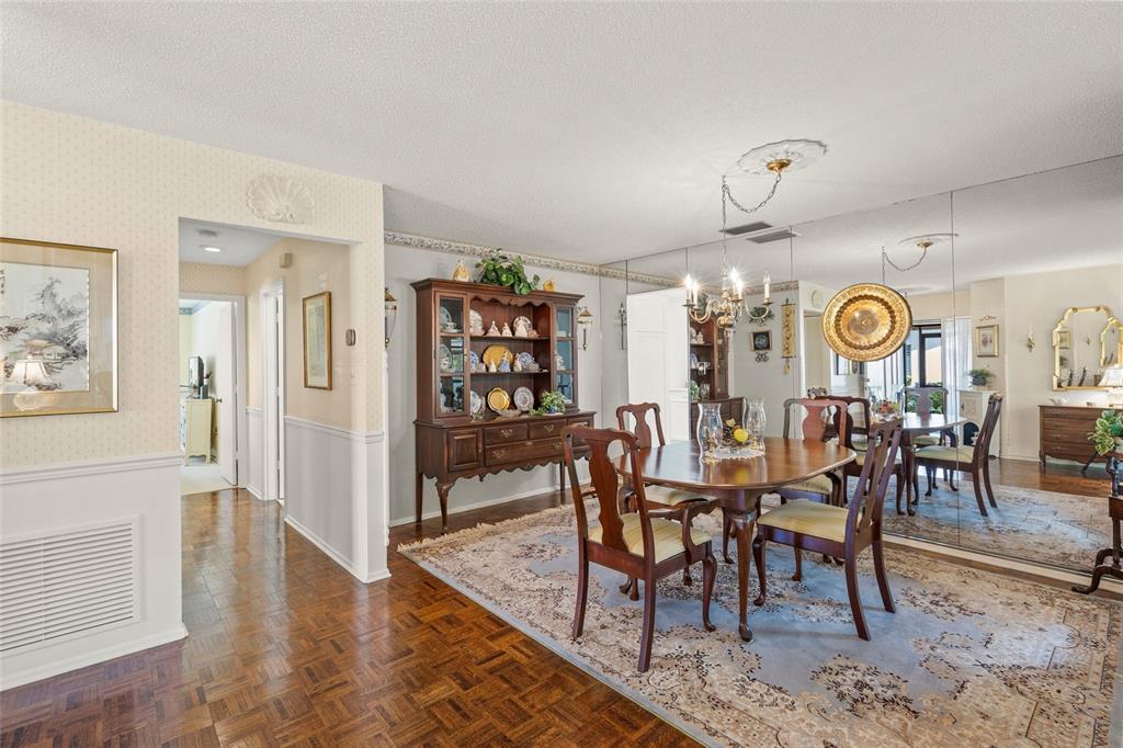 A dining room features a wooden table, a hutch, parquet flooring, and a mirrored wall — 4688 OAK HOLLOW DRIVE UNIT 25, SARASOTA, FL