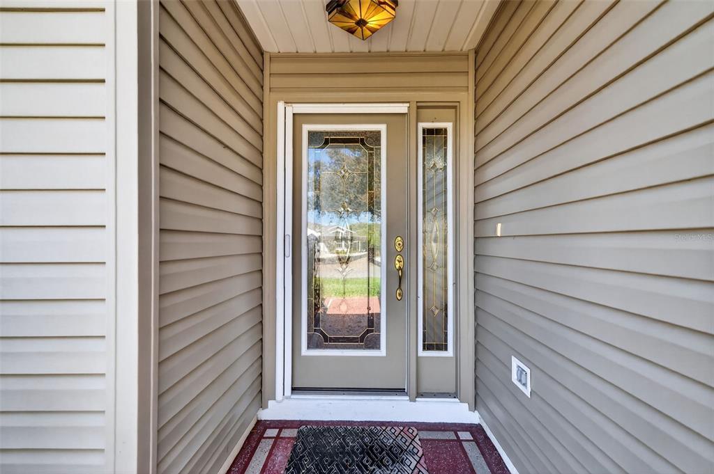 A front entryway features a tan door with a glass insert, sidelight, and beige siding — 17559 SE 81ST PARNASSUS COURT, THE VILLAGES, FL