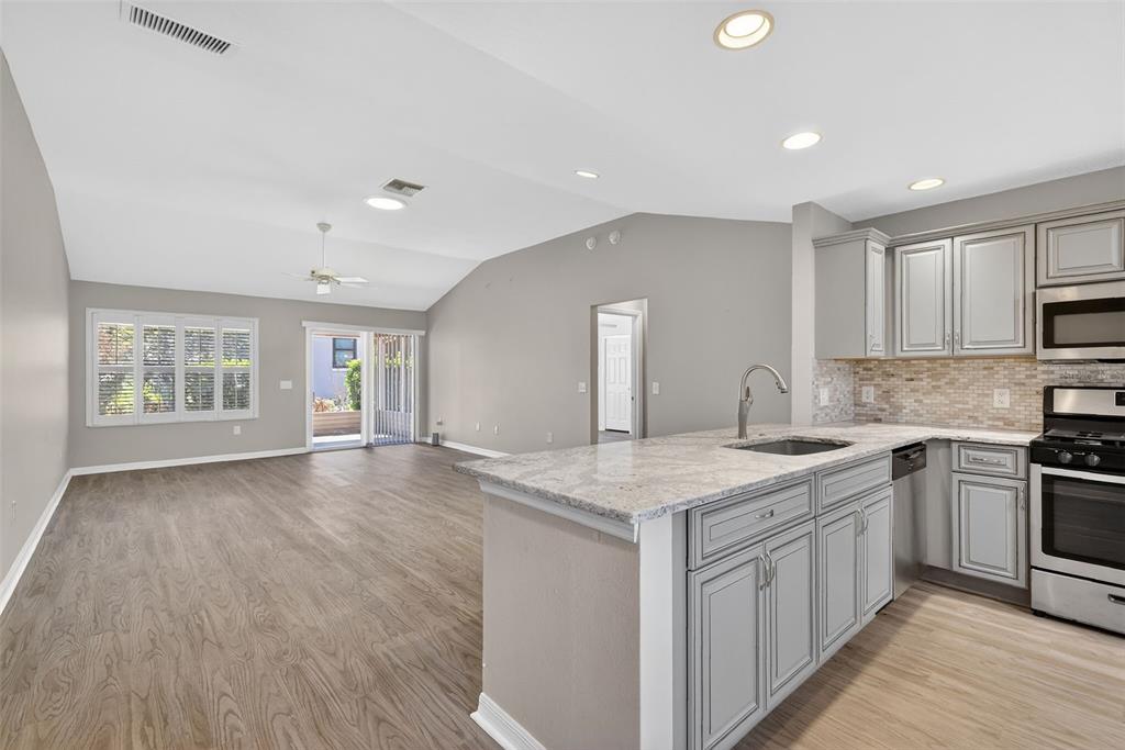 A kitchen with granite countertops and grey cabinets overlooks an open living area with flooring — 17559 SE 81ST PARNASSUS COURT, THE VILLAGES, FL