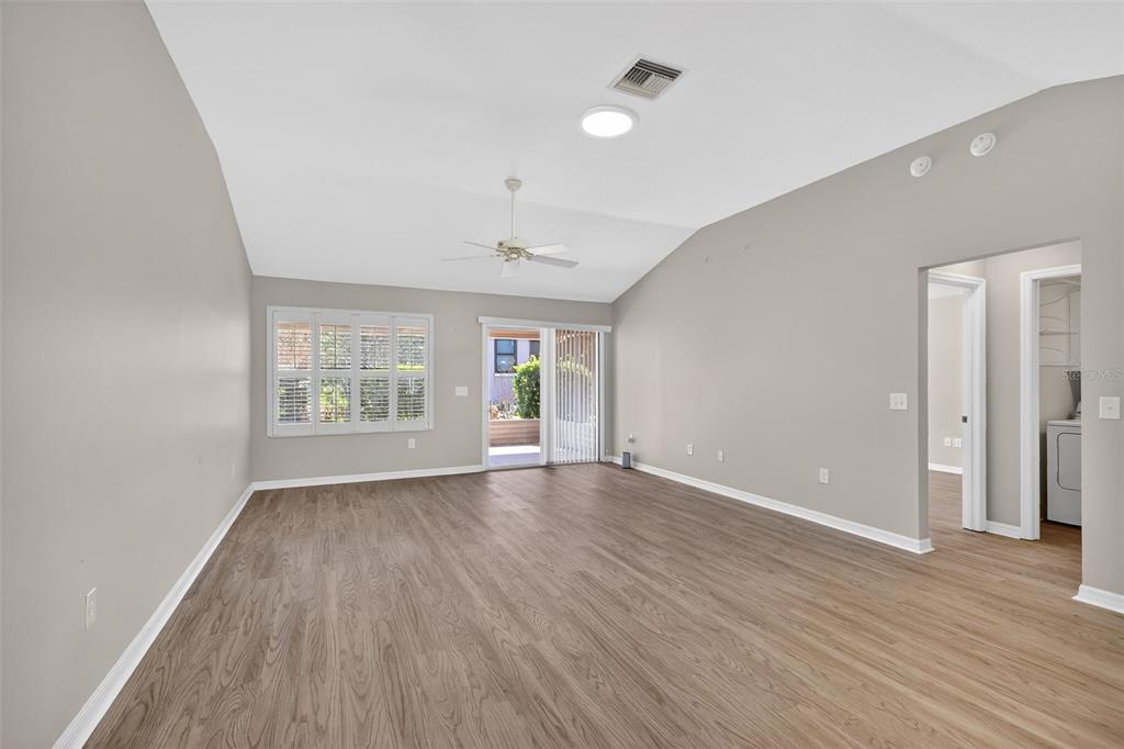 An empty living room with light wood-look flooring, vaulted ceilings, and a sliding glass door — 17559 SE 81ST PARNASSUS COURT, THE VILLAGES, FL