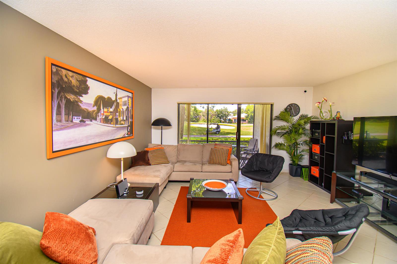 A living room with a sectional sofa, orange rug, and a view of a golf course — 8334 Cypress Lane # 1a, Boca Raton FL 33433, BOCA RATON, FL