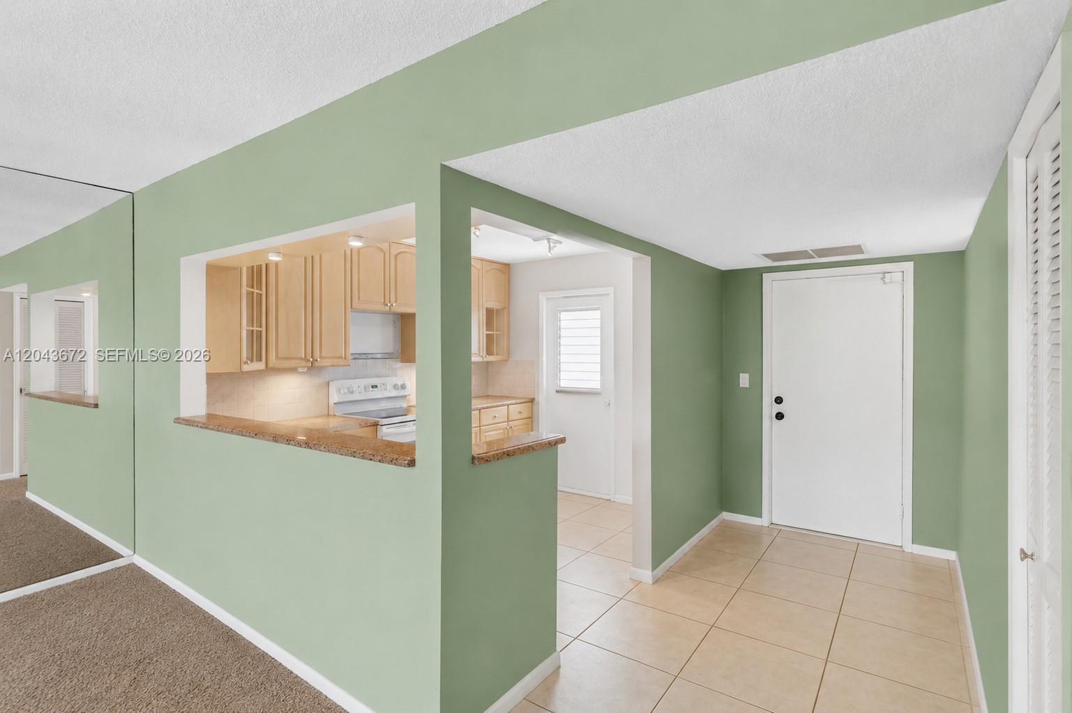 A kitchen with light wood cabinets and a granite countertop opens into a tiled entryway — 3010 N Course Dr # 510, Pompano Beach FL 33069, POMPANO BEACH, FL