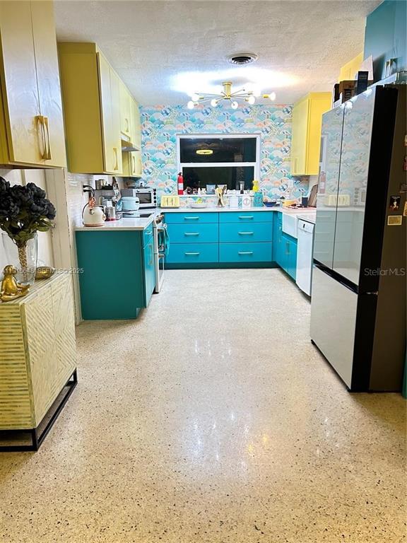 A kitchen features yellow upper cabinets, teal lower cabinets, patterned wallpaper, and terrazzo flooring — 118 BOUGAINVILLEA DRIVE, ROCKLEDGE, FL