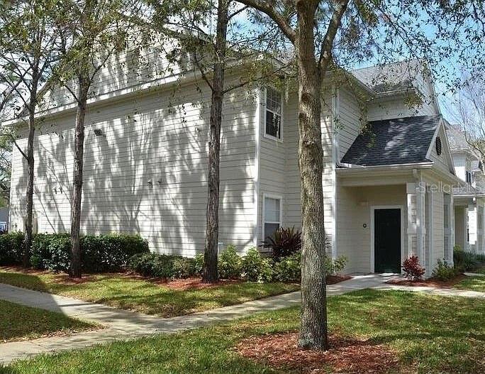 A two-story light-colored siding townhouse with a covered entryway and surrounding trees — 1301 EASTERN PECAN PLACE UNIT 208, WINTER GARDEN, FL