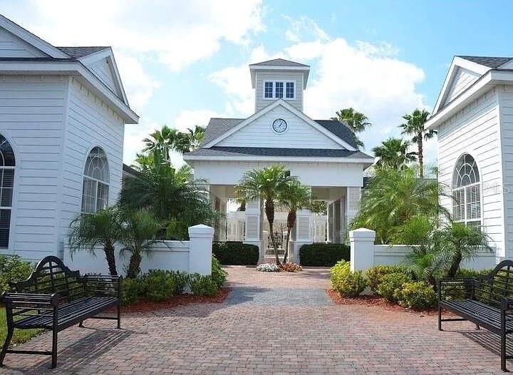 A brick walkway leads to a white building with a clock tower and two benches — 1301 EASTERN PECAN PLACE UNIT 208, WINTER GARDEN, FL