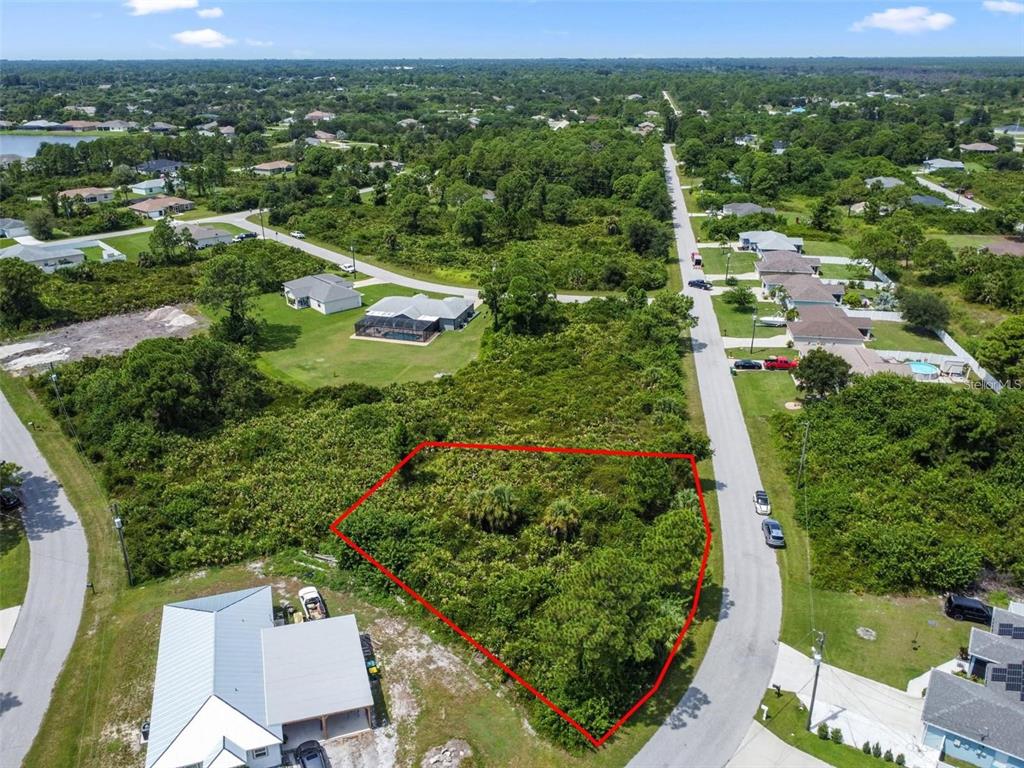 An aerial view shows a vacant, wooded residential lot outlined in red along a paved road — 12447 BIRTLE AVENUE, PORT CHARLOTTE, FL