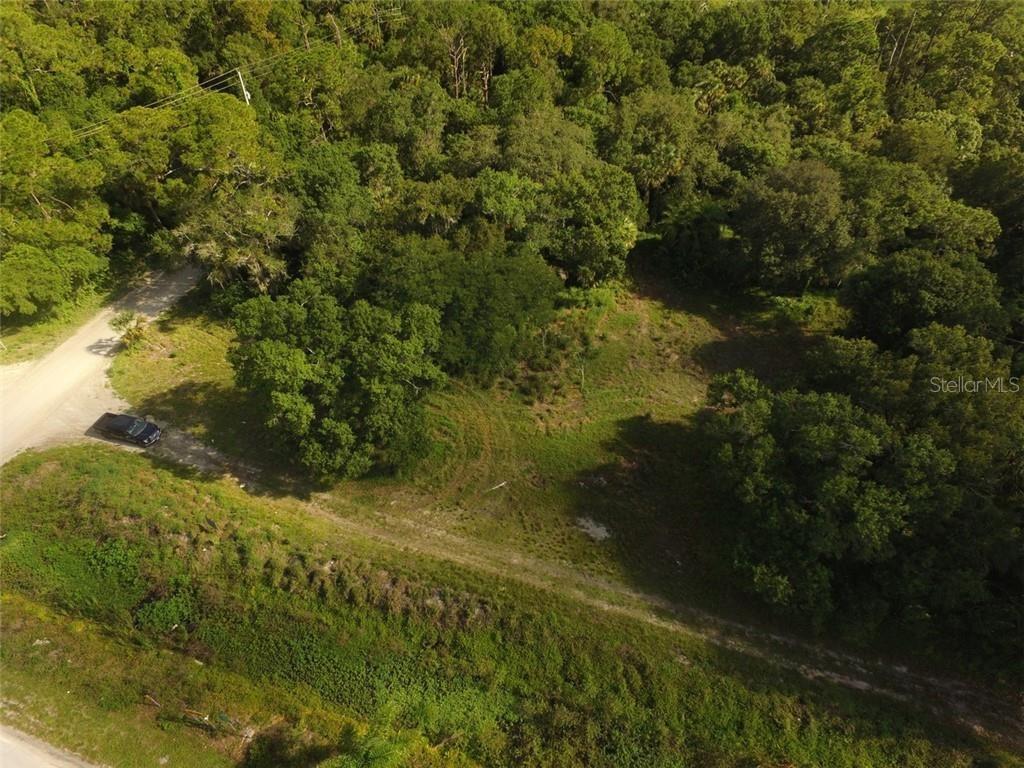 An aerial view shows a cleared, grassy lot surrounded by dense trees and vegetation — 9810 134TH COURT, FELLSMERE, FL