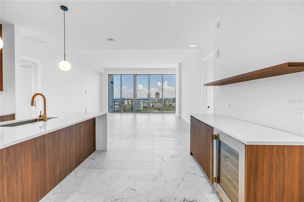 A modern kitchen with white marble floors, wood cabinetry, and floor-to-ceiling windows overlooking a city — 777 3RD AVENUE N UNIT 1704, ST PETERSBURG, FL