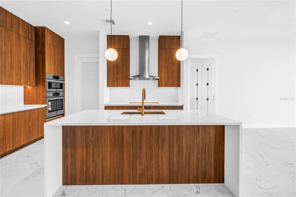 A modern kitchen features wood-grain cabinetry, a white waterfall island, and gold fixtures — 777 3RD AVENUE N UNIT 1704, ST PETERSBURG, FL