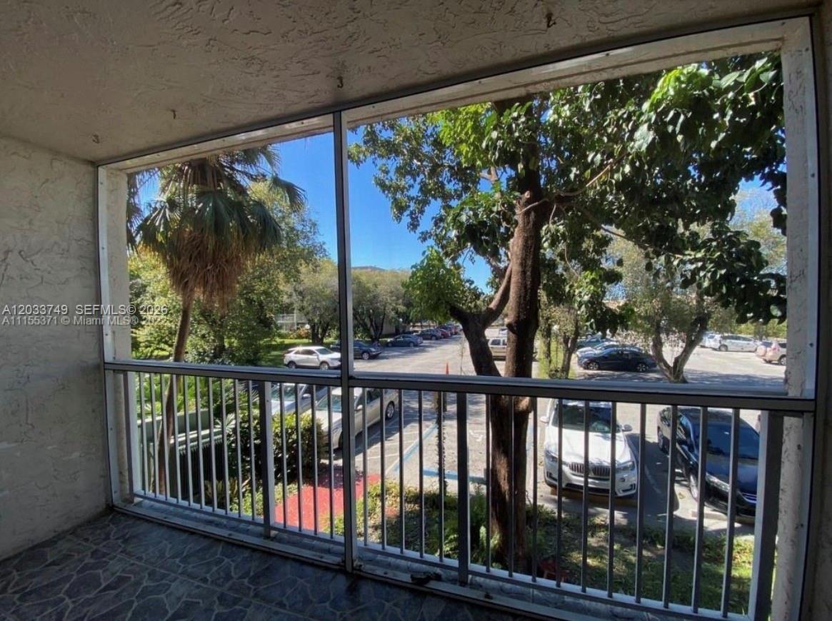 A screened-in balcony overlooks a parking lot with trees and several parked cars — 8421 NW 8th St # 203, Miami FL 33126, MIAMI, FL