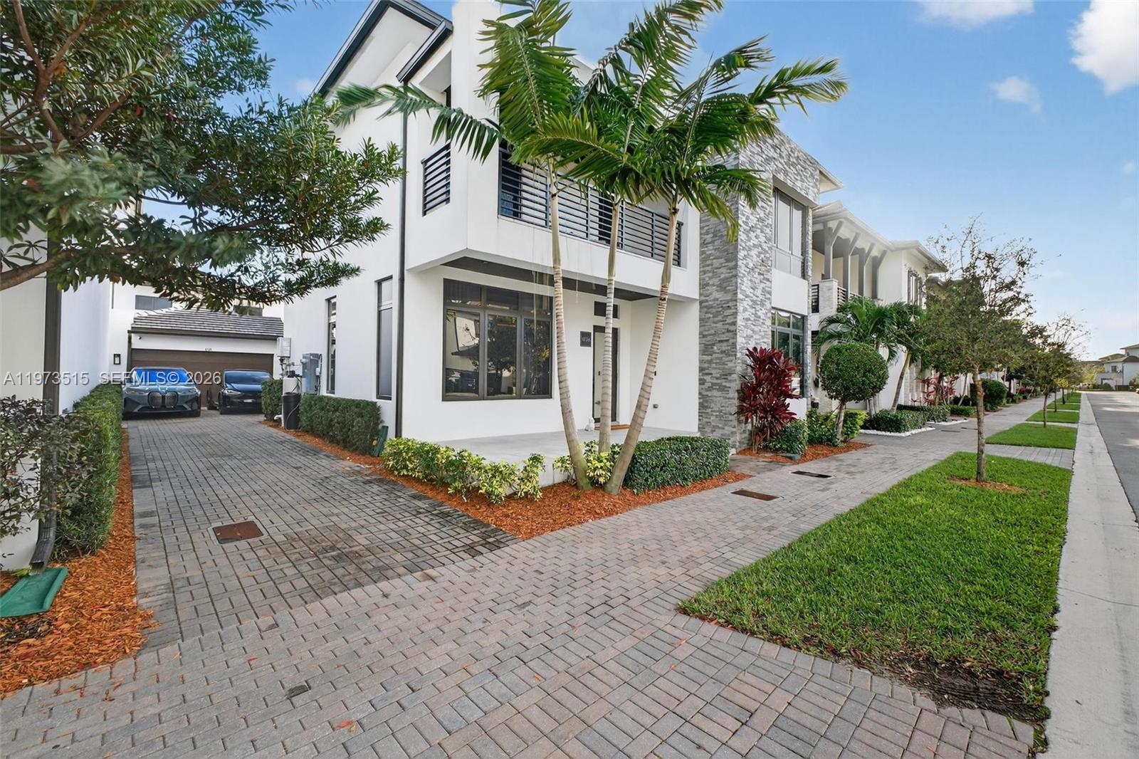 A modern two-story house features a paved driveway, palm trees, and a stone-accented facade — 8126 NW 48th Ter, Doral FL 33166, DORAL, FL