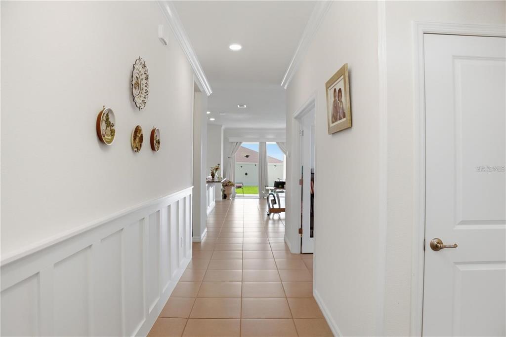 A hallway with tile flooring, white wainscoting, and wall decor leads toward a bright living area — 9152 SW 60TH COURT ROAD, OCALA, FL