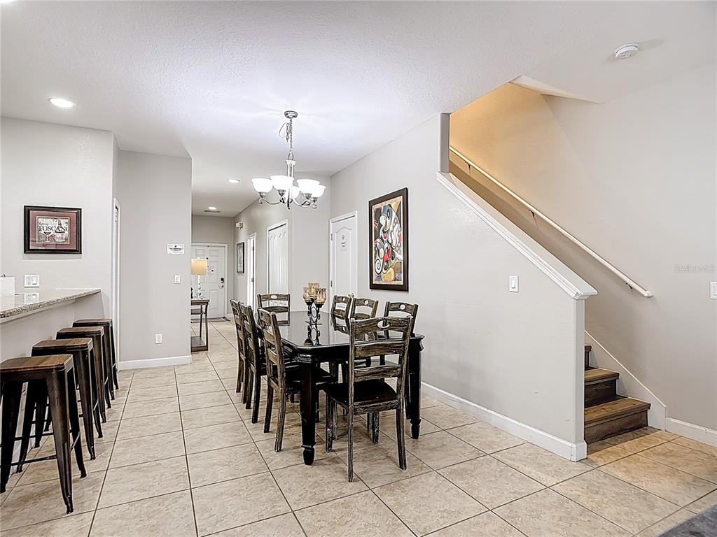 A dining area with a dark table and chairs sits beside a staircase — 8951 CALIFORNIA PALM ROAD, KISSIMMEE, FL