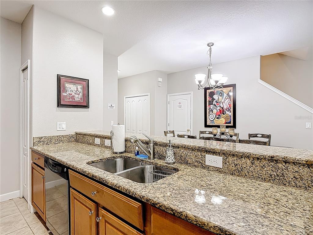 A kitchen sink with granite countertops overlooks a dining area with a Mickey Mouse painting — 8951 CALIFORNIA PALM ROAD, KISSIMMEE, FL
