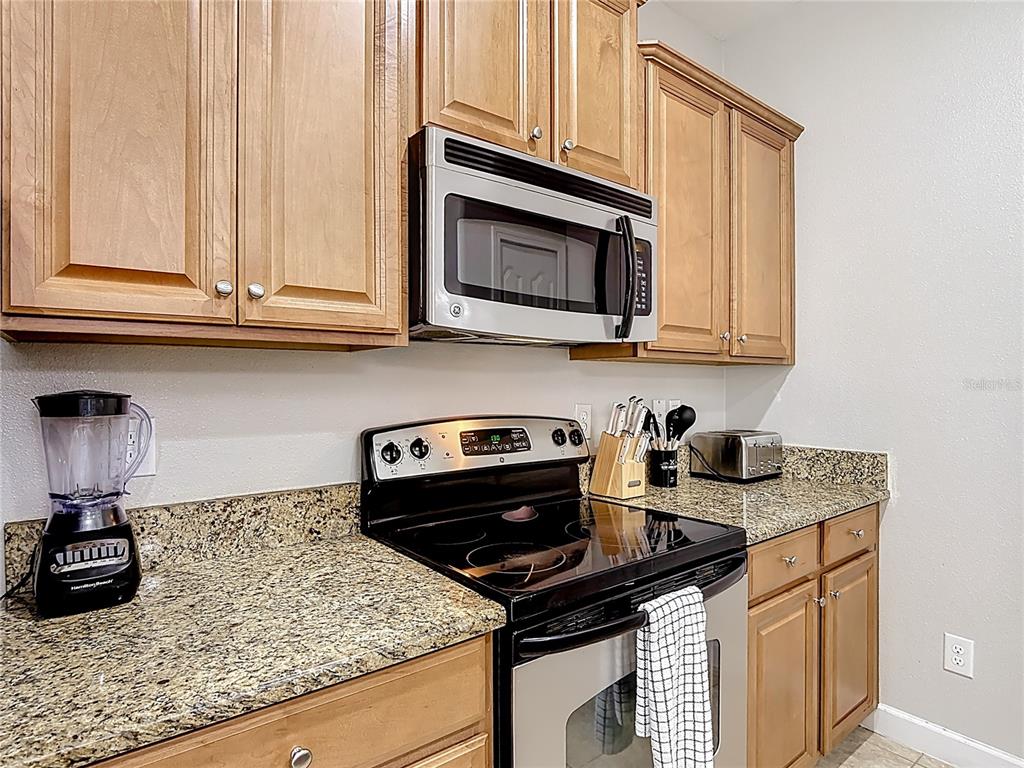 A kitchen features light wood cabinets, granite countertops, a black electric range, and a microwave — 8951 CALIFORNIA PALM ROAD, KISSIMMEE, FL