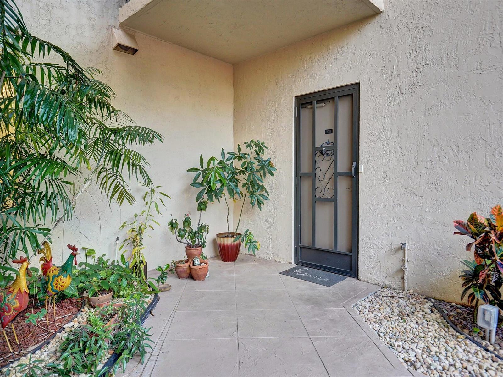 An outdoor entryway features a tiled patio, a metal screen door, and various potted plants — 7546 La Paz Boulevard # 108, Boca Raton FL 33433, BOCA RATON, FL
