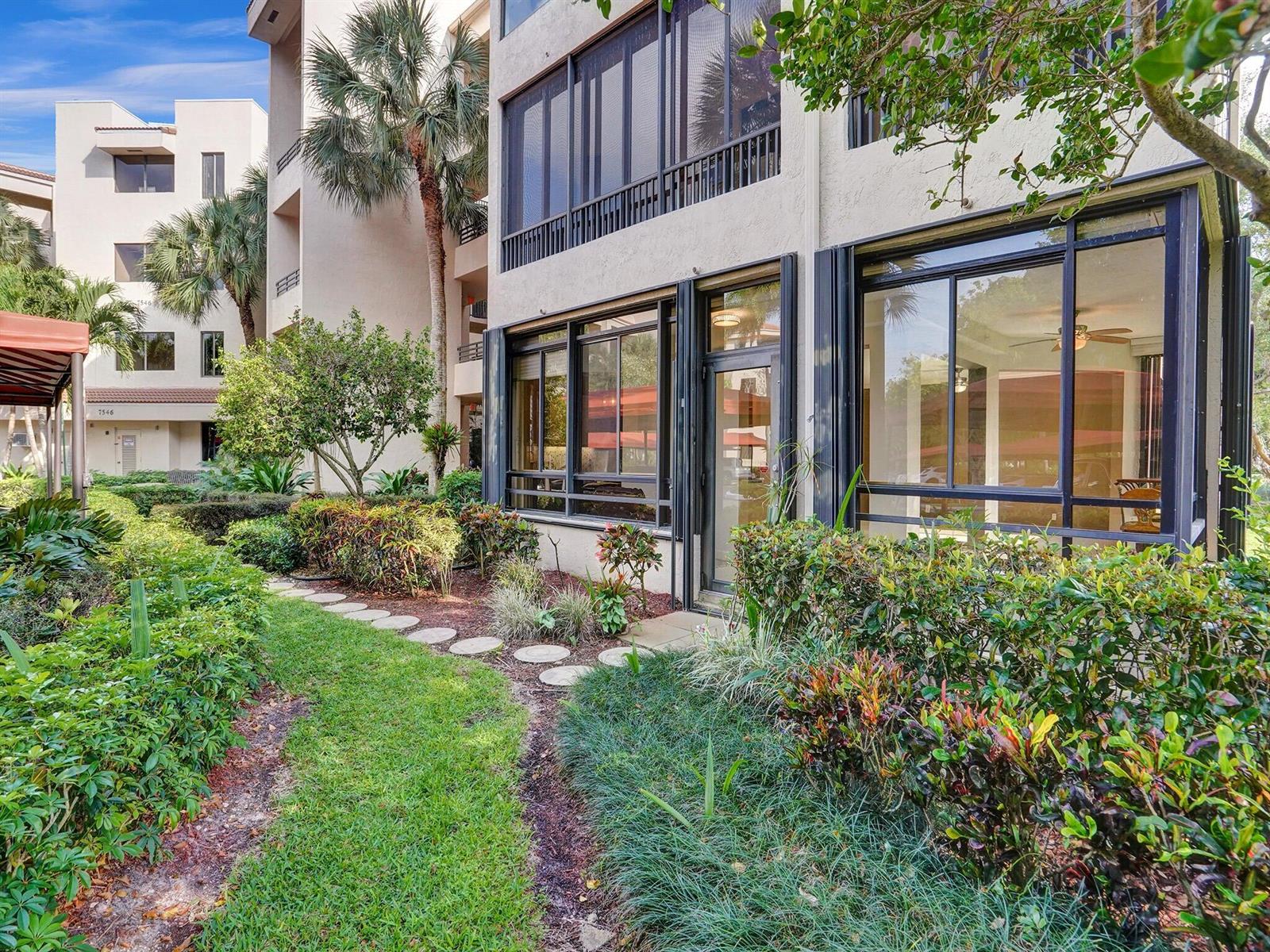 A ground-floor apartment exterior features a screened patio, large windows, and a landscaped garden path — 7546 La Paz Boulevard # 108, Boca Raton FL 33433, BOCA RATON, FL