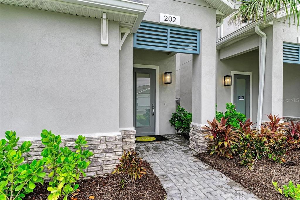 A paved walkway leads to the gray front door of a modern residential building — 10016 REMBRANDT WAY UNIT 202, BRADENTON, FL