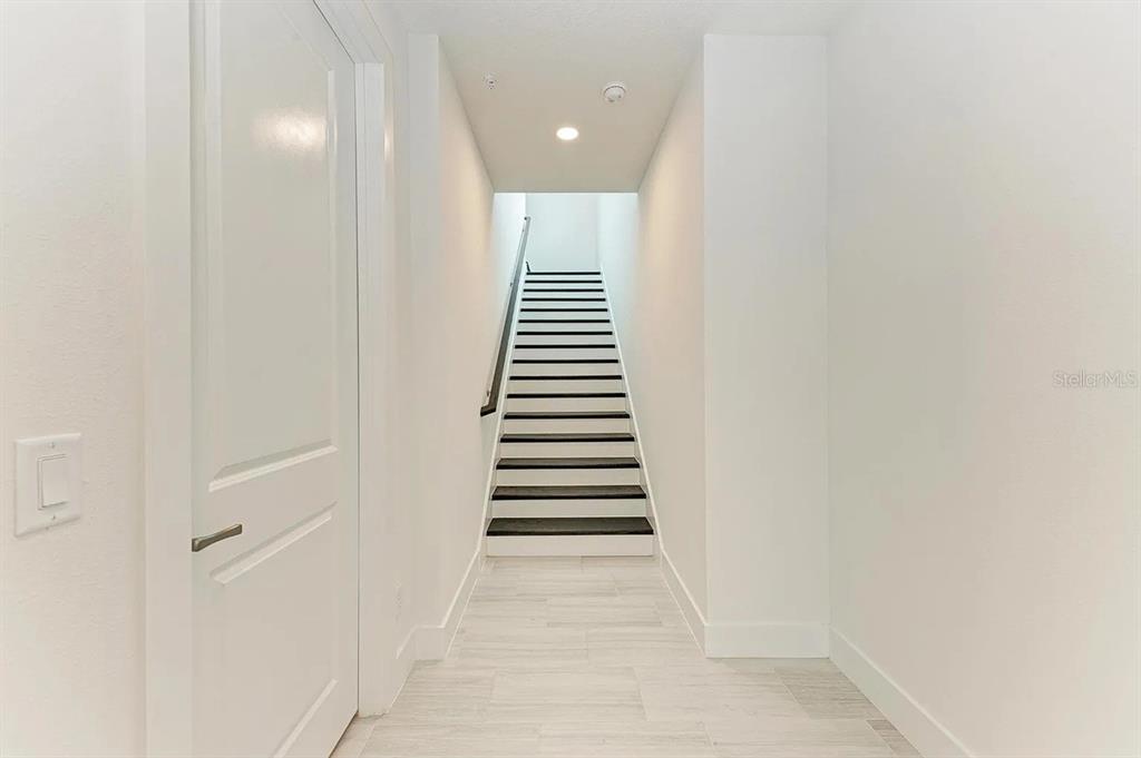 A hallway with white walls and tile flooring leads to a staircase with dark treads — 10016 REMBRANDT WAY UNIT 202, BRADENTON, FL