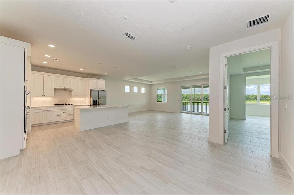 An open-concept kitchen and living area with white cabinetry, tile flooring, and a glass door — 10016 REMBRANDT WAY UNIT 202, BRADENTON, FL