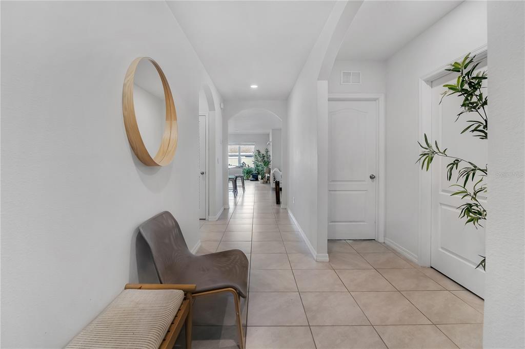 A tiled hallway features a round mirror, a modern chair, and white interior doors — 9009 PINALES WAY, KISSIMMEE, FL