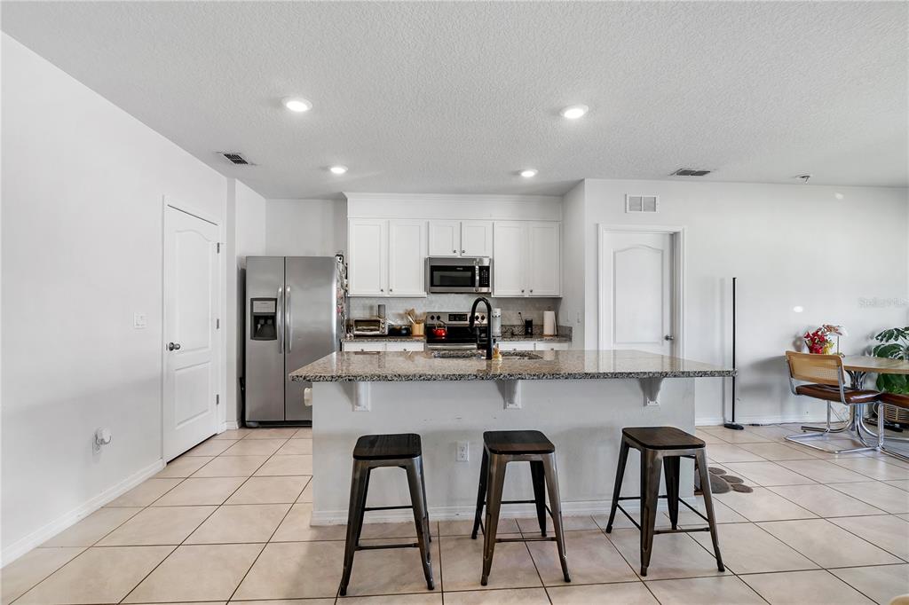 A kitchen features white cabinets, stainless steel appliances, a granite island, and three bar stools — 9009 PINALES WAY, KISSIMMEE, FL
