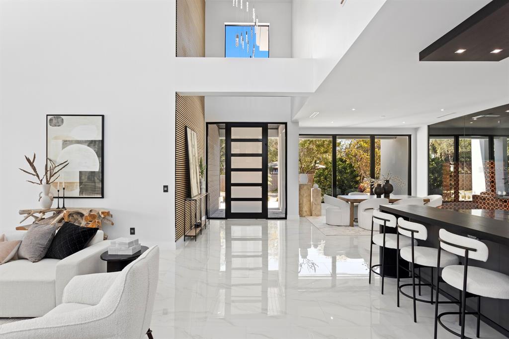 A modern, open-concept living area features white marble floors, high ceilings, and a glass-paneled front door — 2089 ARLINGTON STREET, SARASOTA, FL