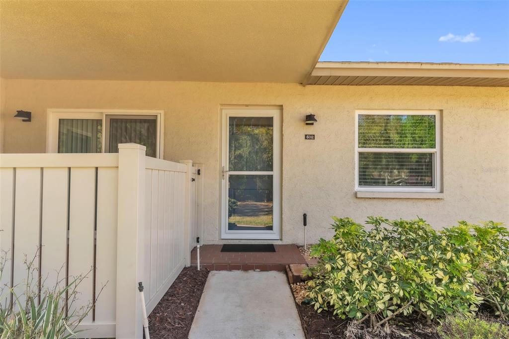 A beige exterior wall features a front door with a screen, a window, and fencing — 600 S WOODLANDS DRIVE, OLDSMAR, FL
