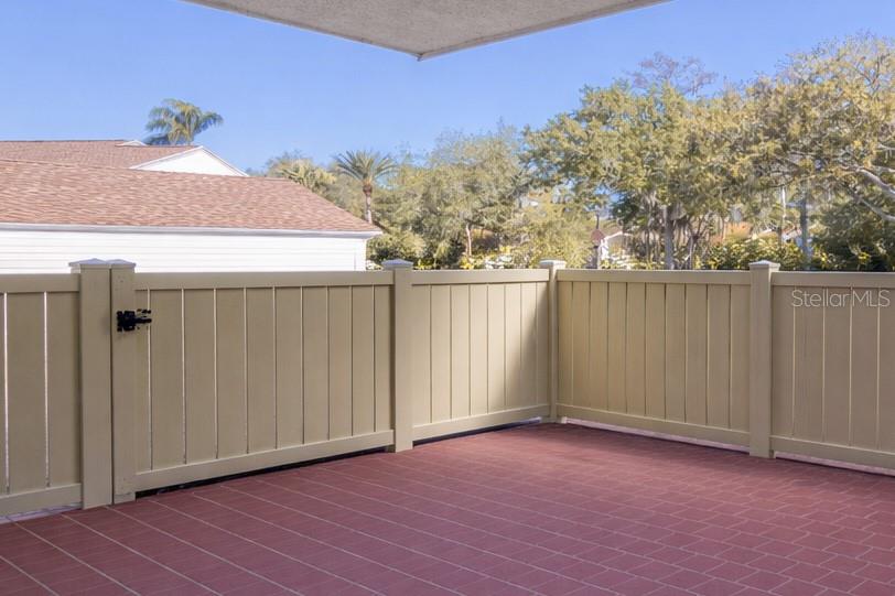 A patio with red tile flooring and a tan vinyl privacy fence — 600 S WOODLANDS DRIVE, OLDSMAR, FL
