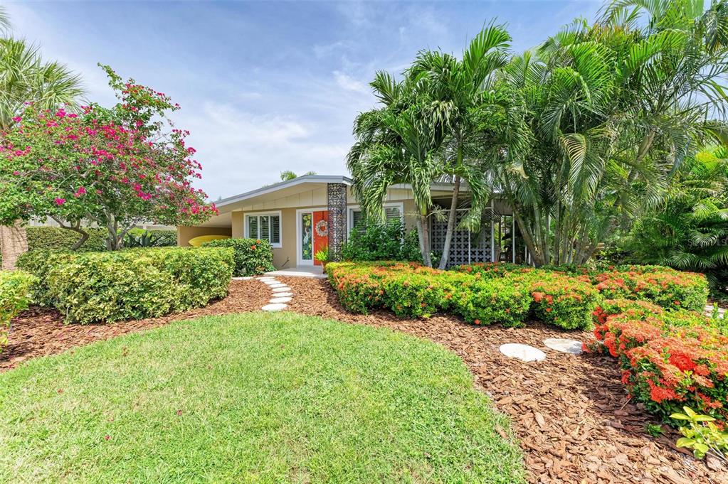 A single-story house with a bright orange front door, palm trees, and landscaped garden beds — 136 CRESCENT DR, ANNA MARIA, FL