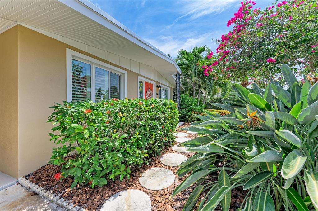 A tan house exterior features a front garden with a stone path and flowering plants — 136 CRESCENT DR, ANNA MARIA, FL