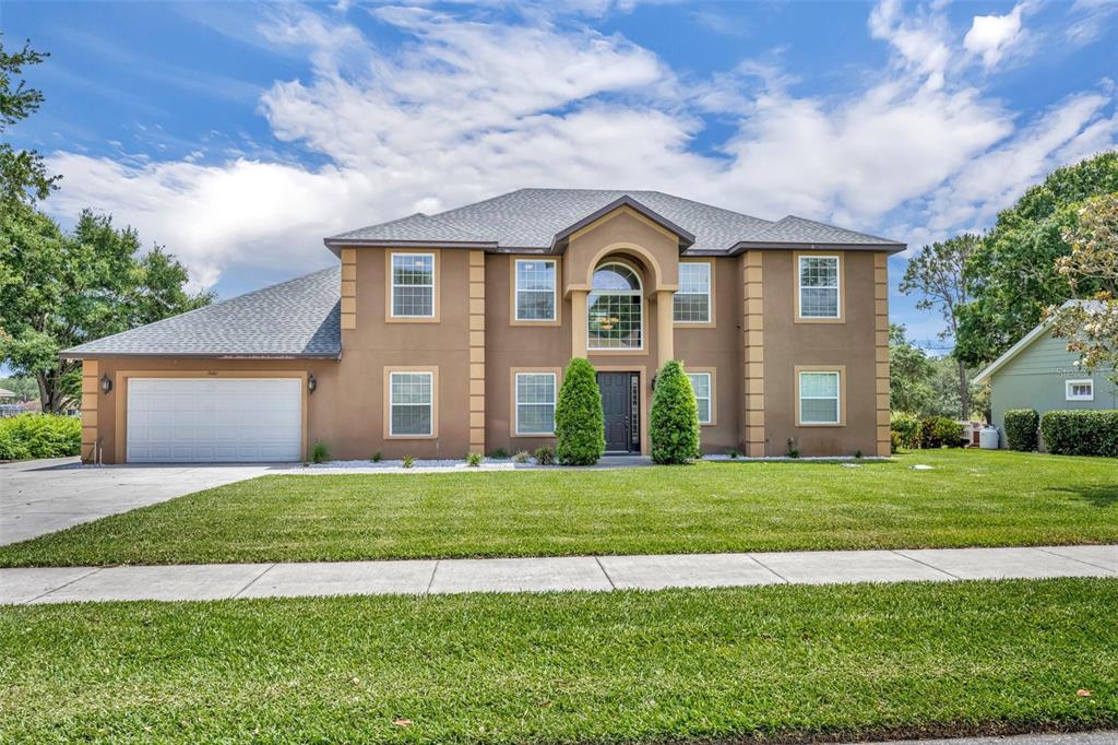 A two-story tan stucco house with a gray shingled roof and a two-car garage — 15001 GREEN VALLEY BOULEVARD, CLERMONT, FL
