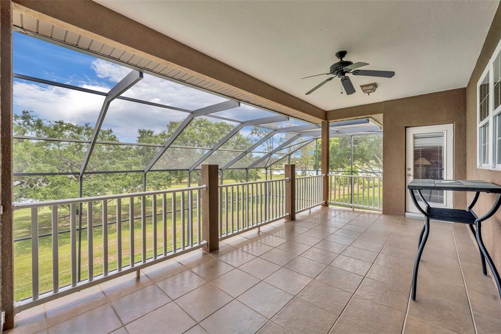 A tiled, screened-in porch features a ceiling fan, metal railings, and views of a grassy yard — 15001 GREEN VALLEY BOULEVARD, CLERMONT, FL
