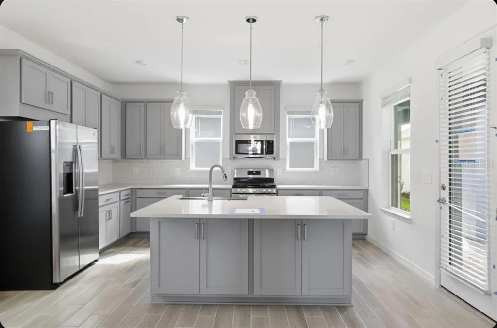 A modern kitchen features gray cabinets, a white quartz island, stainless steel appliances, and pendant lighting — 5174 DOMINION ALLEY, ST CLOUD, FL