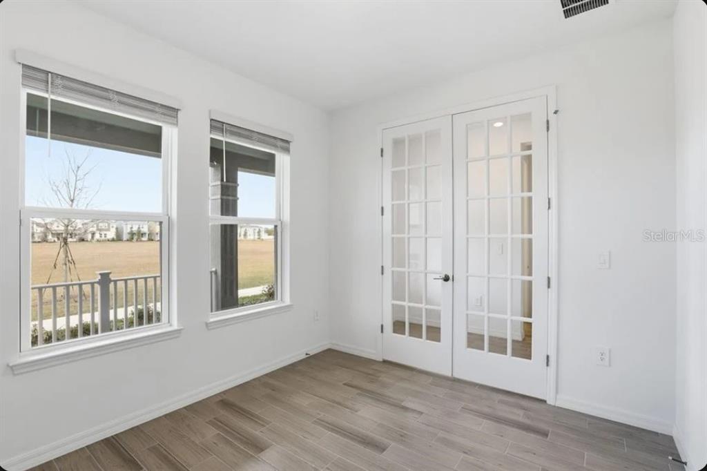 An empty room with white walls, wood-look tile flooring, two windows, and white French doors — 5174 DOMINION ALLEY, ST CLOUD, FL
