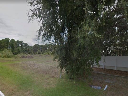 A vacant, grassy residential lot features a large tree and a white vinyl privacy fence — 249 BOUNDARY BOULEVARD, ROTONDA WEST, FL