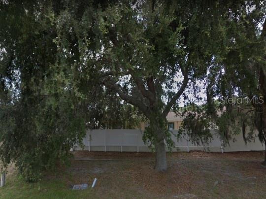 A large tree stands in front of a white privacy fence and a house exterior — 249 BOUNDARY BOULEVARD, ROTONDA WEST, FL