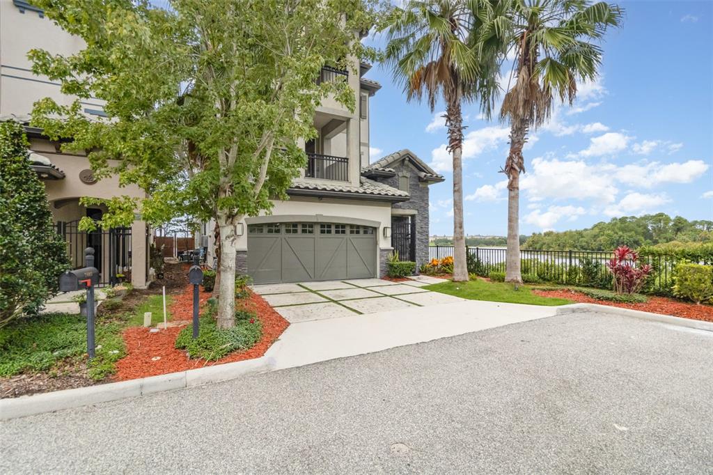 A multi-story house with a two-car garage, palm trees, and a view of a lake — 7601 TOSCANA BOULEVARD, ORLANDO, FL