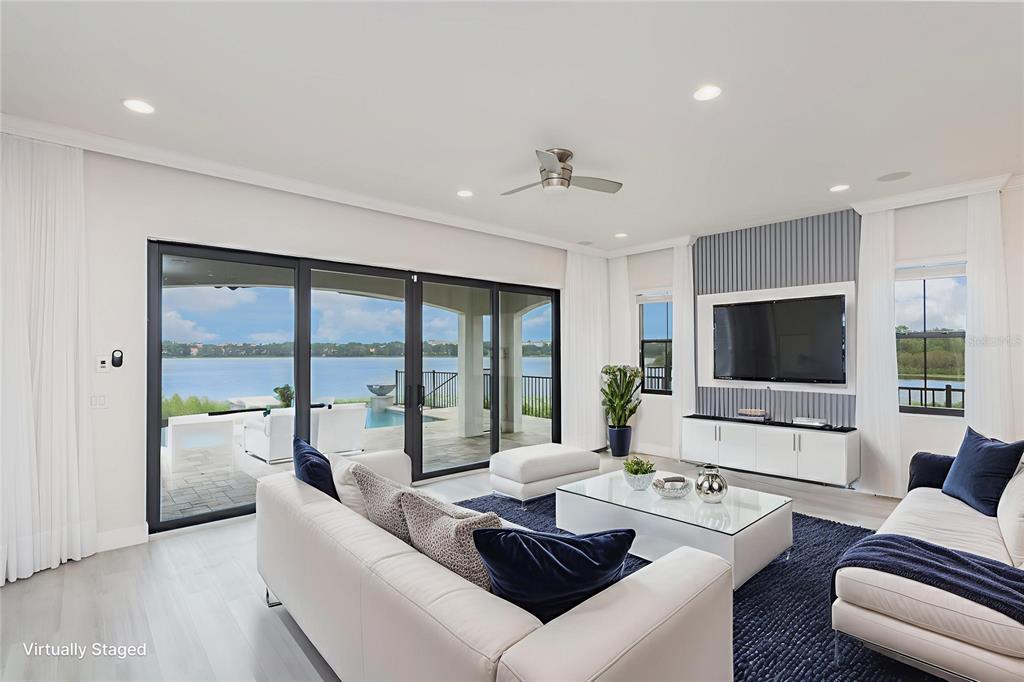 A living room with white sofas, a glass coffee table, and sliding doors overlooking water — 7601 TOSCANA BOULEVARD, ORLANDO, FL