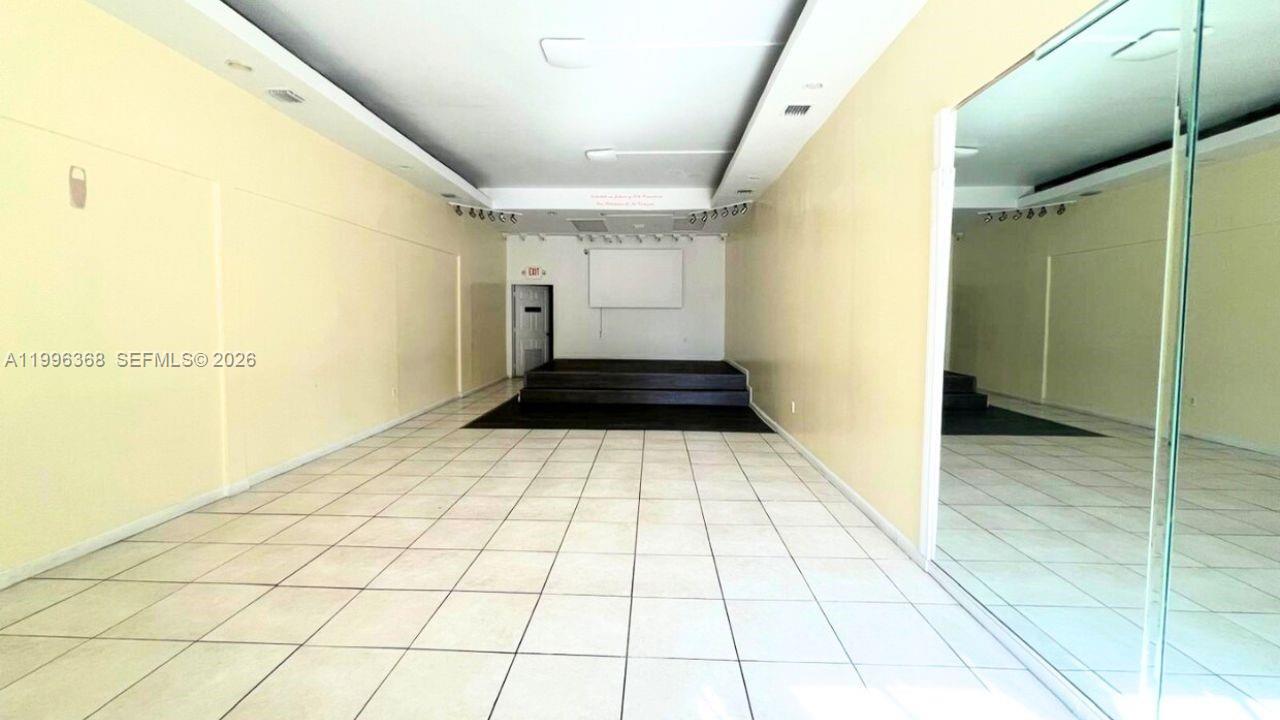 A long, empty room features light-colored tile flooring, a raised stage, and a large mirror — 2617 W Flagler St, Miami FL 33135, MIAMI, FL