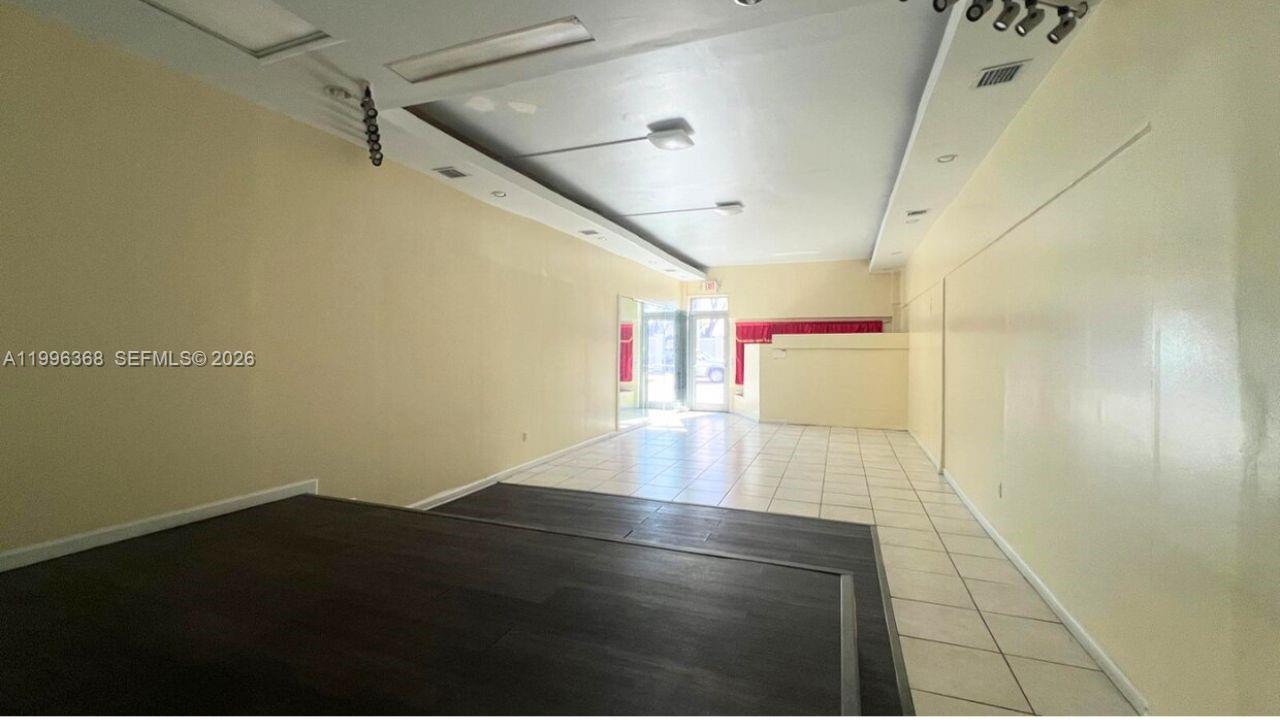 An empty commercial space features a dark wood-look platform, tiled flooring, and beige walls — 2617 W Flagler St, Miami FL 33135, MIAMI, FL