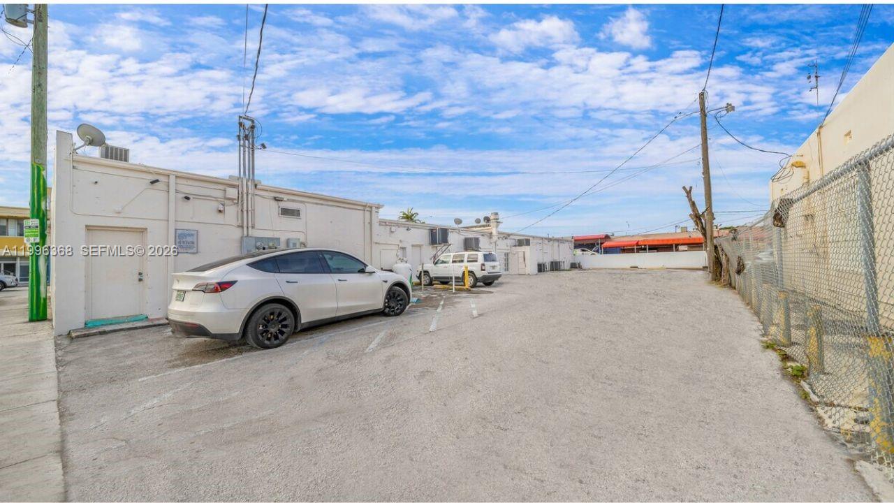 A white car is parked in a paved lot next to a low-rise commercial building — 2617 W Flagler St, Miami FL 33135, MIAMI, FL