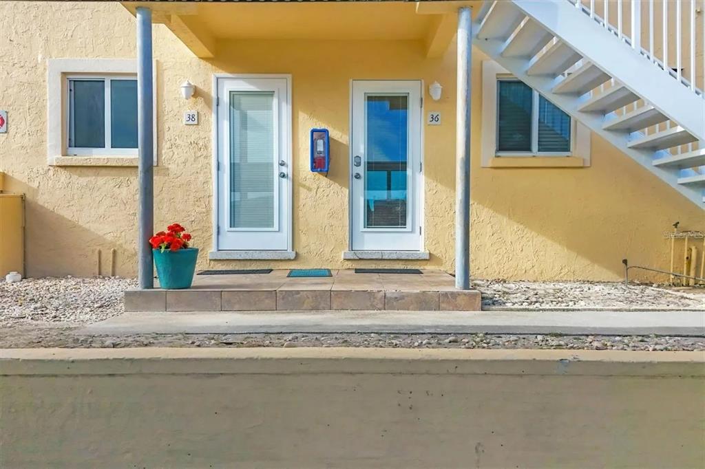 The exterior of a yellow building features two adjacent doors, a staircase, and a planter — 6006 MIDNIGHT PASS ROAD UNIT 36, SARASOTA, FL