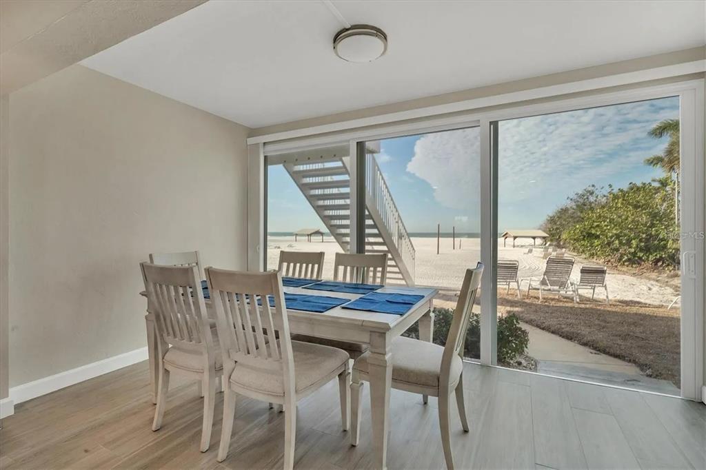 A dining area with a wooden table and chairs overlooks a beach through sliding doors — 6006 MIDNIGHT PASS ROAD UNIT 36, SARASOTA, FL