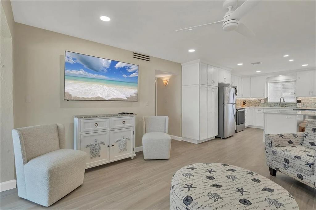A living room with light tile floors, a wall-mounted television, and an open-concept kitchen — 6006 MIDNIGHT PASS ROAD UNIT 36, SARASOTA, FL