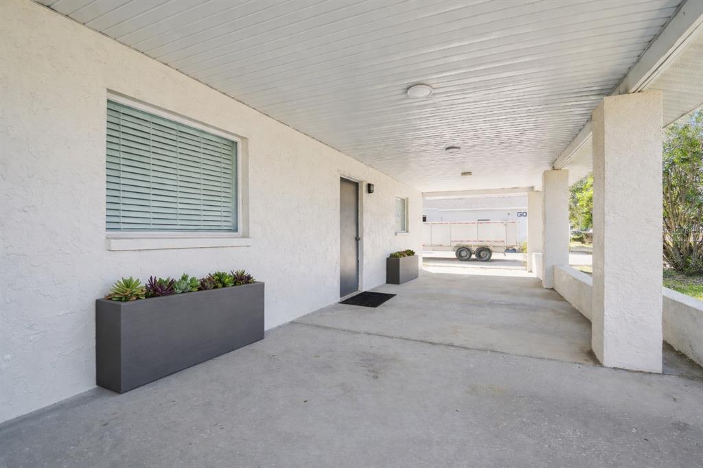 A covered concrete walkway features white stucco walls, a gray door, and two rectangular planters — 6010 WALL STREET, PORT RICHEY, FL