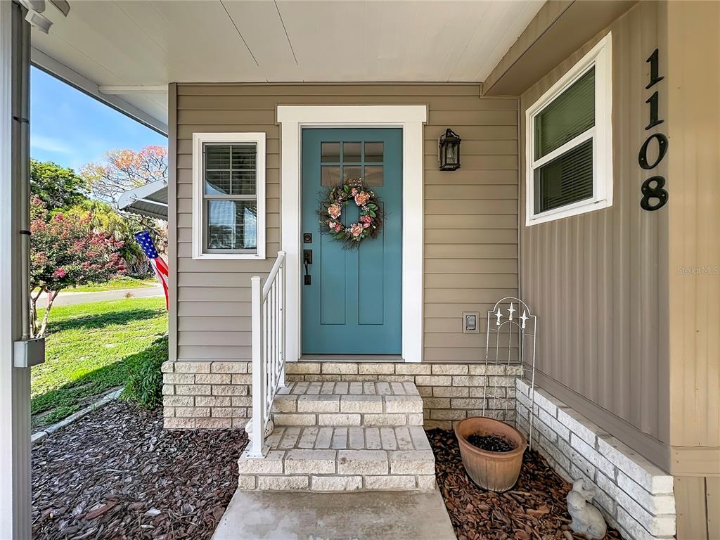 A teal front door with a wreath sits at the top of brick steps — 1108 NASSAU CIRCLE, TAVARES, FL